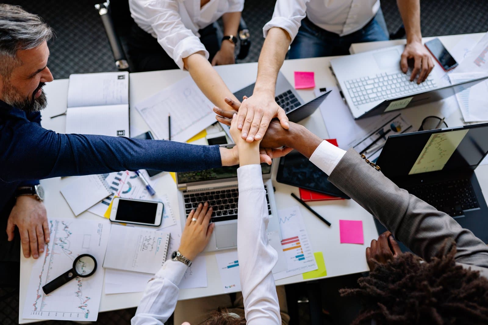 A cross-functional team joining hands over a project desk